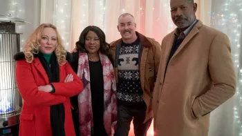 Four middle aged adults stand together in winter coats inside a soft-lit room. The women are caucasian and African American as are the men 