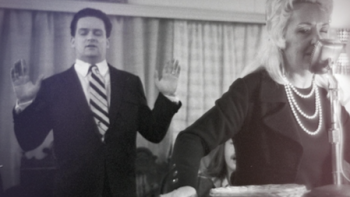 How I Escaped My Cult screenshot 1: A young Tony Alamo in suit raises hands while Susan Alamo preaches on microphone wearing pearls.