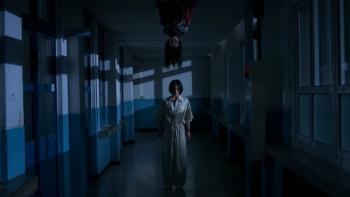 If Wishes Could Kill screenshot 3: A girl in a jumpsuit walks a dark hallway seemingly oblivious to the figure hanging upside-down from the ceiling
