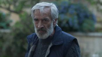  Imanol Arias. He wears a dark cable knit sweater and blue zip vest.