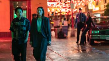 Interior Chinatown TV show screenshot 2: Willis and Lana walk together down a Chinatown street, glowing with a red light; behind them is a man staring