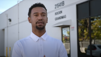 Jury Duty Company Retreat TV show screenshot 2: Anthony is interviewed in front of a white building wall with "Rockin Grandmas" on one wall