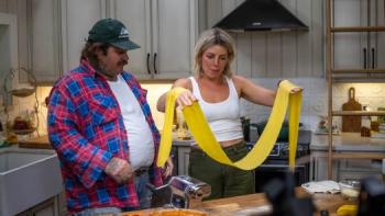 Just a Dash TV show screenshot 1: Matty Matheson and Michelle Rabin stand at a kitchen island. Rabin holds out a large strip of pasta across her arms.