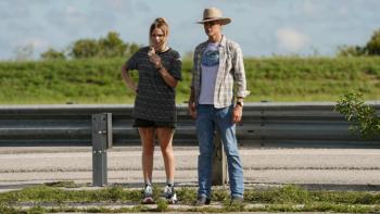 Justified: City Primeval: Willa and Raylan stand together on the side of a highway, looking at something off-camera. Willa is in shorts, Raylan is in jeans, a plaid Western shirt, and a cowboy hat. 