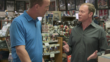 King of Collectibles: The Goldin Touch screenshot 3: Payton Manning in blue shirt stands left while talking to Ken Goldin on right in the markeplace. 