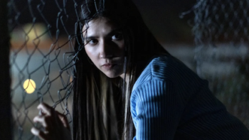 La chica invisible TV show screenshot 3: Aurora looks over shoulder before climbing through wire fence at night. 