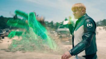 Lanterns: Guy Gardner, in a Green Lantern costume, strides across a barren landscape as a huge green glowing hand lights up behind him 