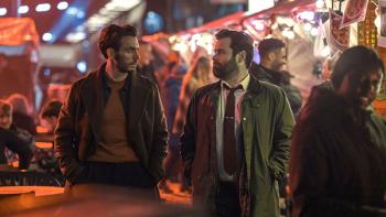 Laz and Seth look at each other while walking through an outdoor night market
