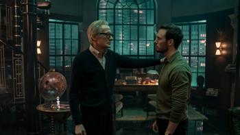 Dr. Jonathan Lazarus stands facing his son Joel, hand resting on his shoulder, in front of the desk in his moodily-lit Art Deco-style office