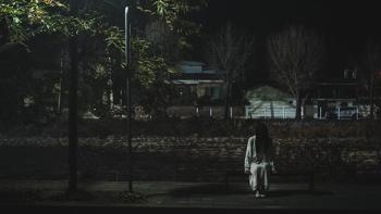 Light Shop TV show screenshot 1: A woman in white clothing sits on a bus stop bench in the dark, her head bowed and long black hair obscuring her face