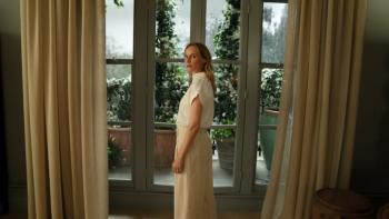 Little Disasters TV show screenshot 1: Jess stands in front of a window in an elegant room in a long white dress