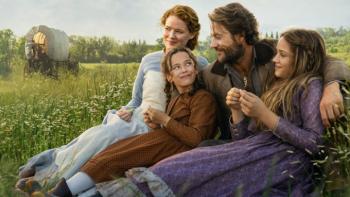 Little House on the Prairie TV show: Mary, Laura, Charles, and Caroline sit close together on a green stretch of prairie, their wagon behind them
