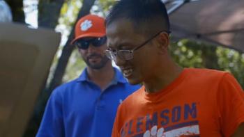 Living Undocumented Series: Two men in Clemson sports gear smile as they cook at a barbecue.