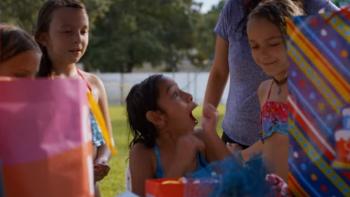 Living Undocumented Series: A small girl looks ecstatic as she opens a present at a birthday party. 