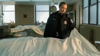Long Bright River TV show poster: Actress Amanda Seyfried, a white blonde woman wearing a police uniform, looks under a sheet in a morgue