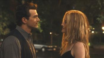 Love Story screenshot 1:Paul Anthony Kelly and Sarah Pidgeon stand in the night. Kelly wears a gray shirt and black vest. Pidgeon wears a black dress.