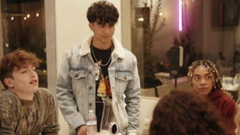 Love ALLways screenshot 2: Male contestant wears jean jacket and stands next to table where others are sitting. 