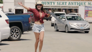Luanne & Sonja: Welcome to Crappie Lake TV show screenshot 2: LuAnn runs through parking lot in white short and purple low cut blouse, hat, sunglasses. 