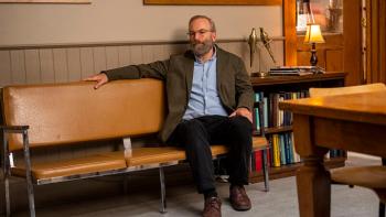 Lucky Hank TV show: Hank sits on a wooden bench dressed in a jacket and button down shirt; he appears to be dismayed