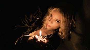 Lucky TV show screenshot 3: Anya Taylor-Joy lays down in the dark on her side. She holds a lighter in her hand, flame alit. She wears a black jacket.