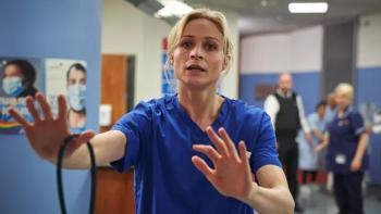 Malpractice TV show screenshot 2:Niamh Algar holds her hands out in a calming gesture. She wears blue scrubs and is holding a stethoscope in one hand.