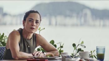 Man on Fire TV show screenshot 3: Alice Braga sits a restaurant table. She wears an olive green sleeveless top and a gold necklace.