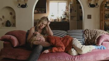 Michelle Pfeiffer sits on a velvet couch, with Elle Fanning laying her head on her lap.