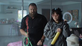 Nick Offerman and Thaddea Graham. Offerman wears a black shirt with red graphics. Graham wears a grey coat and pink glasses.