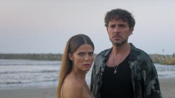 Medusa TV show screenshot 1: Juana Acosta and Manolo Cardona stand on a beach. Acosta wears a dress, Cardona in a black tank top and floral button up.