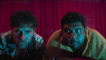 Medusa TV show screenshot 2: JManolo Cardona and Johan Rivera huddle in front of a red curtain, wearing ear buds.