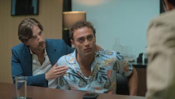 Medusa TV show screenshot 3: Carlos Torres and Sebastian Osorio sit. Torres wears a dark blue blazer and white shirt. Osorio wears a floral shirt.