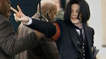 Michael Jackson: The Verdict TV show screenshot 1: Michael Jackson in a black suit flashes a peace sign.