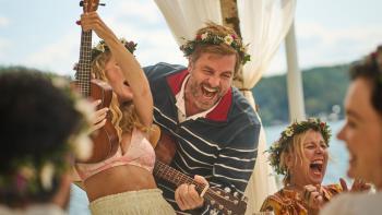 Midsummer Night TV show screenshot 2: Midsummer celebration party guests in floral crowns sing and play the ukulele