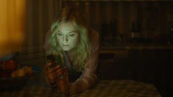 MILF of Norway TV show screenshot 3: In a dark room, Lene bends over and leans onto a table, her face illuminated