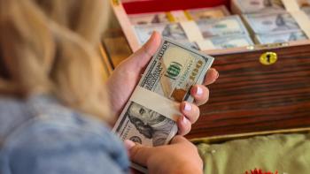 Millionaire Dollar Secret: close up shot of a women's hands holding a stack of money above a box of money.
