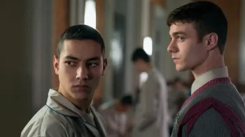 Minerva Academy TV show screenshot 1: Salvo looks over his shoulder as if intimidated while Diego masks his discomfort in a dimly lit room.