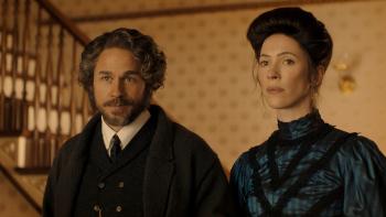 The Lizzie Borden Story screenshot 2: Charlie Hunnam and Rebecca Hall. Hunnam wears a black coat, vest, and tie. Hall wears a black and blue dress.
