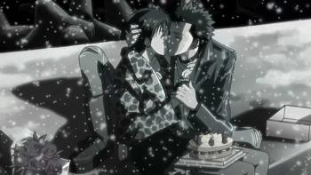 Nana: A black and white flashback image of Nana O. kissing Ren outside in the snow. They sit on a ledge. Nana has a cake in her lap.