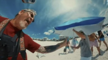 Neighbors TV show screenshot 3: A man records himself with a selfie stick while people aim a beach umbrella in his direction.