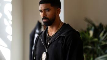 Matthew Law. He wears a black zip up jacket and a black shirt. Around his neck he wears a gold chain, and a police badge.