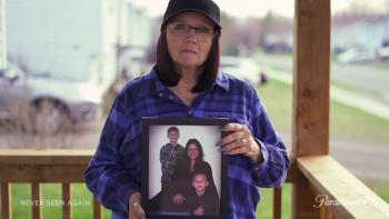 Never Seen Again TV show screenshot: A White lady frowns while holding up a picture of a family.