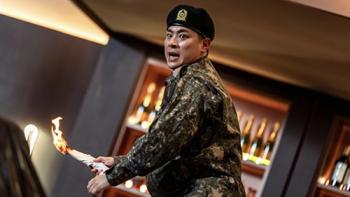 Newtopia TV show screenshot 2: Jae-yoon wears his military uniform while standing in front of a bar, about to throw a rolled-up napkin that's on fire