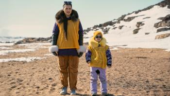North Of North TV show screenshot 3: Siaja and daughter, Bun, stand in the beach wearing yellow sports vests on a bright sunny day.