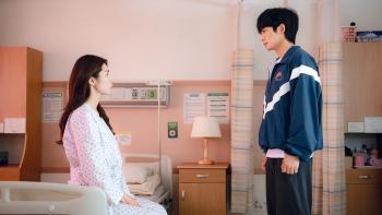 Ha-young and Jung Hae-in. Ha-young sits on a hospital bed, wearing patient attire. Jung wears a blue jacket and sweatpants.