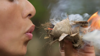 Outlast: The Jungle TV show screenshot 2: Woman blowing on fire-starting bundle outdoors.