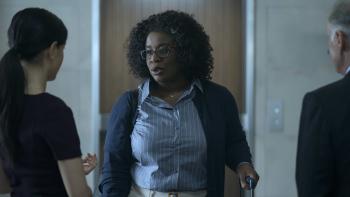 Painkiller TV Show Screenshot 1: Uzo Aduba as Edie Flowers, holding a suitcase in one hand. She speaks to two others in the foreground.