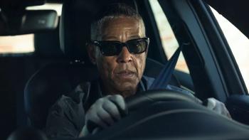 Giancarlo Eposito as Parish sits behind the wheel of a car wearing sunglasses and grey driving gloves