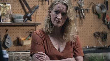 Paula Malcomsen as Rose stands in front of a pegboard full of tools, her arms crossed and wearing rust-colored t-shirt