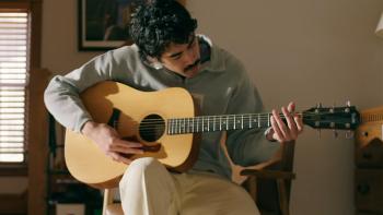 People Like Me TV Show screenshot 2: Daren Vongirdner strums a wooden guitar. He wears a light grey quarter-zip sweater and khaki pants.