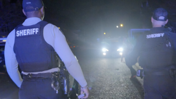 Police 24/7 TV show screenshot 3: Two sherriffs with vests walk towards headlights of vehicle 